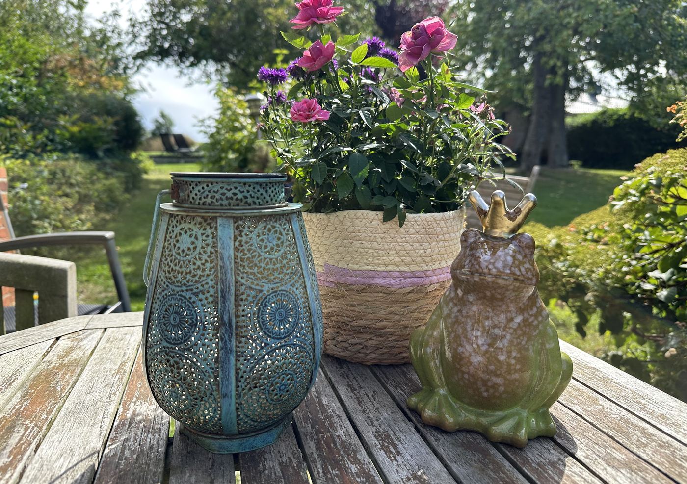 Laterne, Rosen im Korb und ein Froschkönig aus Keramik auf dem Gartentisch