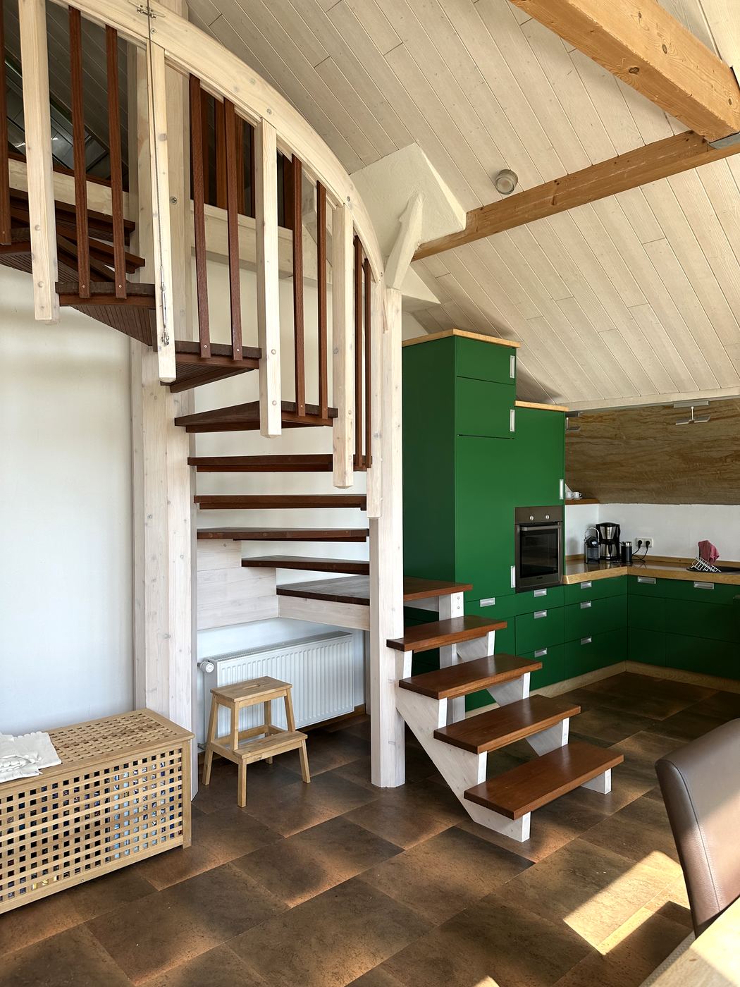 Wendeltreppe aus hellem Holz neben der grünen Küche