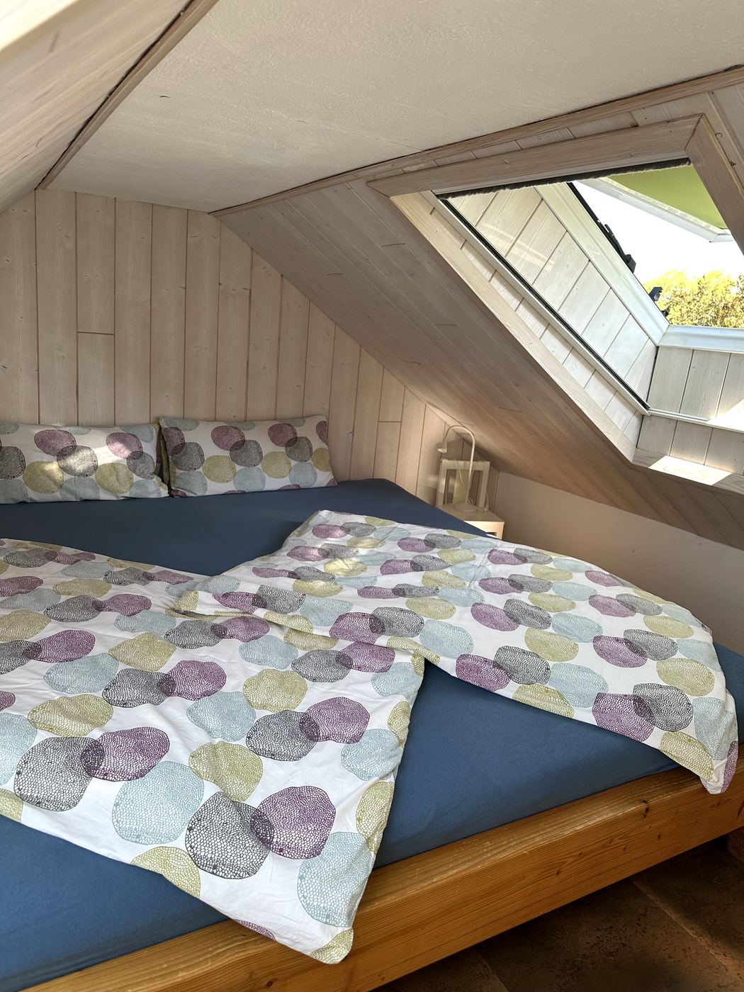 Das geöffnete Dachfenster über dem Bett, dahinter Baumkronen