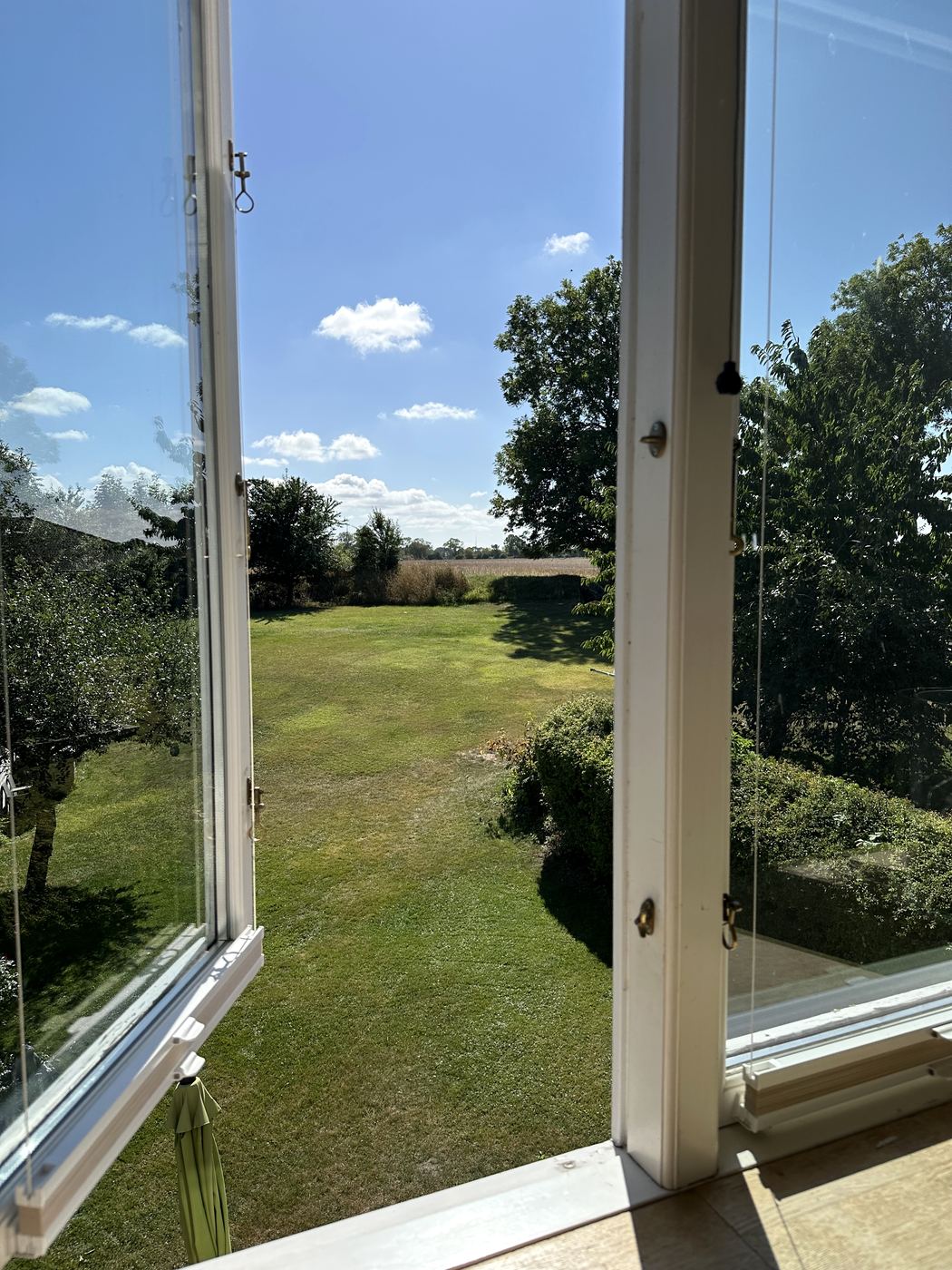 Blick aus dem geöffneten Fenster über den Rasen bis zum Feld