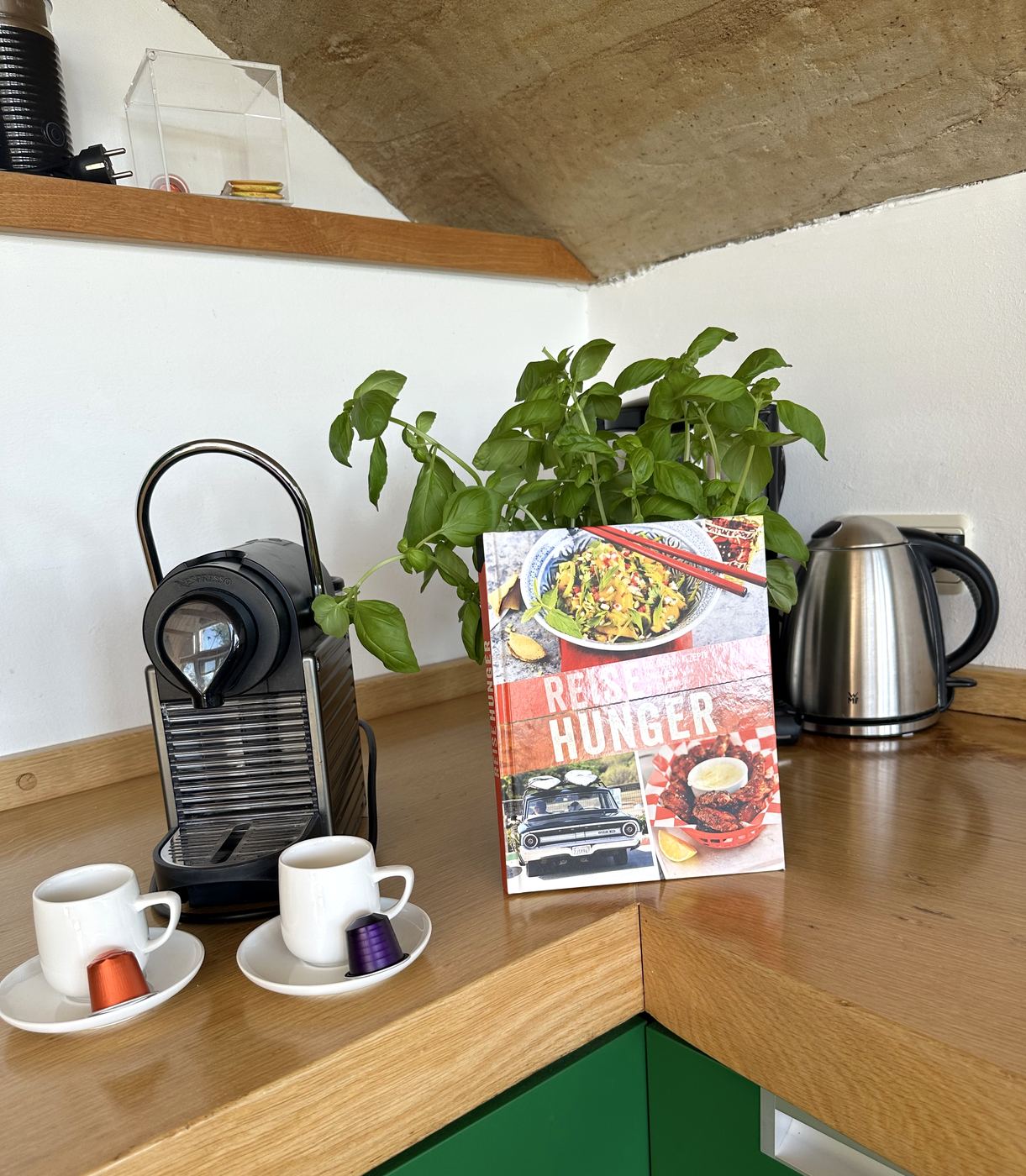 Nespresso-Maschine, Wasserkocher, Basilikum und Kochbuch auf der Arbeitsplatte