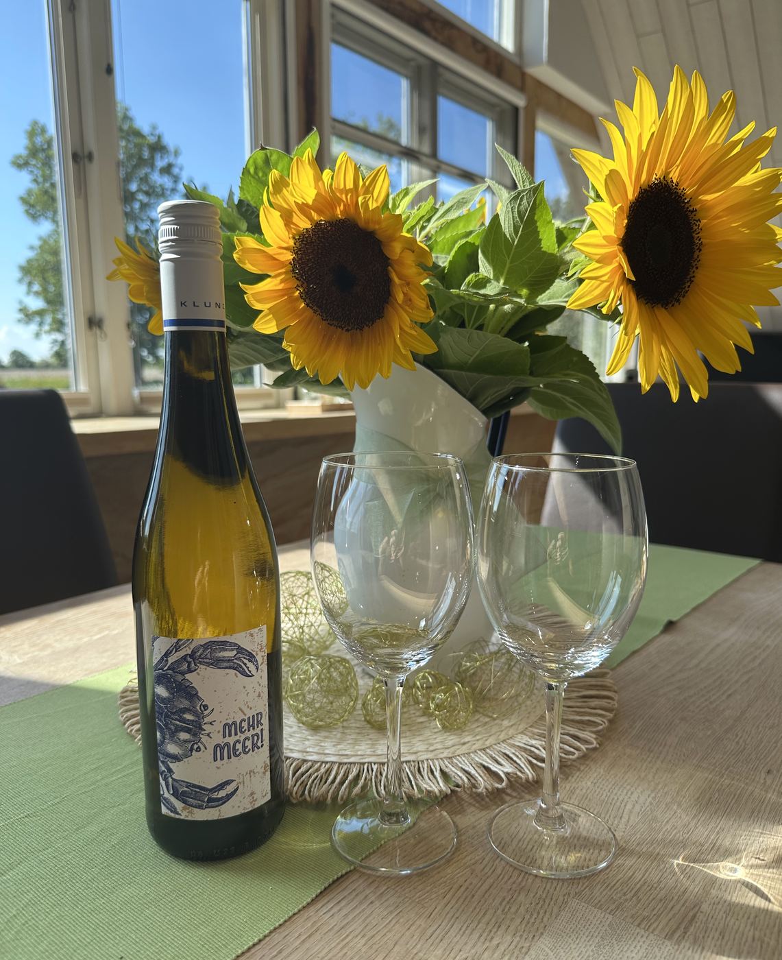 Weinflasche, zwei Gläser und Sonnenblumen auf dem Esstisch