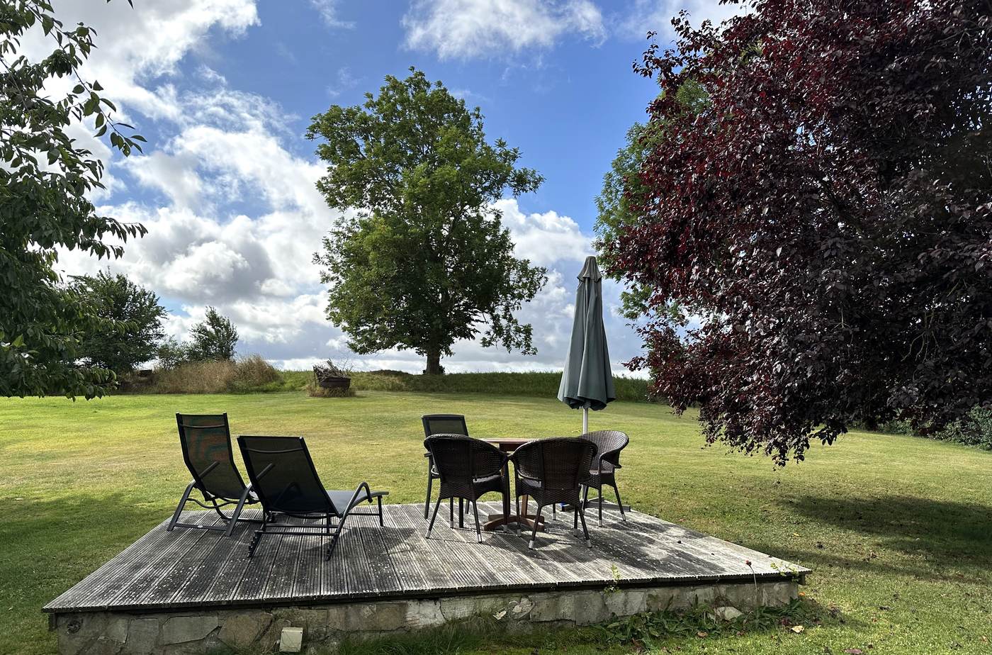Holzterrasse im Garten mit Liegen, Tisch, Stühlen und Sonnenschirm
