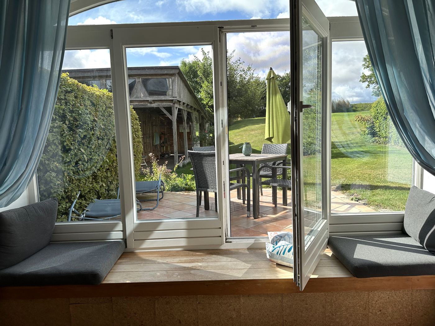 Blick von der gepolsterten Fensterbank durch die offene Terrassentür in den Garten